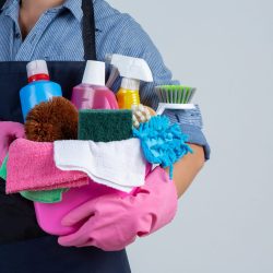 Young girl is holding cleaning product, gloves and rags in the basin on white background